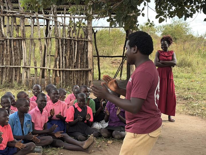 A YKMI team member teaching a group of children seated outdoors