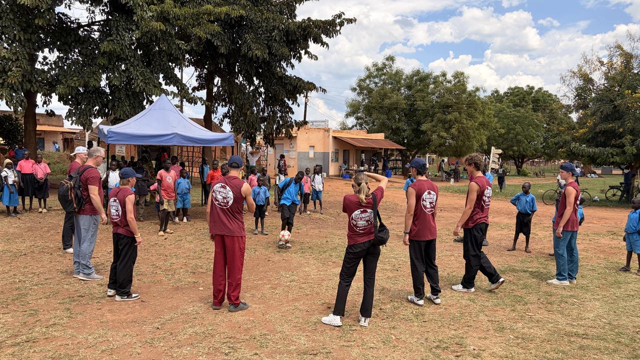 Outreach team members in maroon shirts with children on an open field beside a blue tent